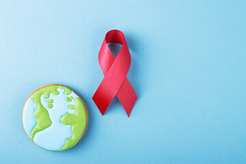 Red ribbon and gingerbread planet earth on a blue background. The concept of world cancer day
