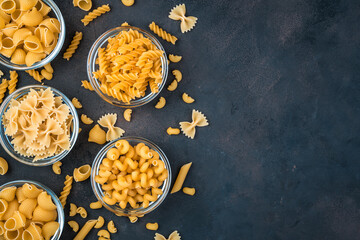 Assortment of pasta in bowls on a dark concrete background. Top view, with space to copy. Concept of products, culinary backgrounds.