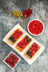 top view berry waffles on white rectangular plate bowls of pomegranate and raspberries colorful xmas toys on grey-white background