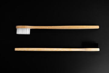 Two Eco-friendly antibacterial bamboo wood toothbrushes with white and black bristles on a black background. Taking care of the environment is trending. Tolerance. Copy space