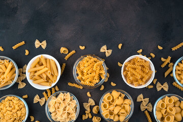 Bowls of pasta of different varieties on a dark concrete background. Top view, with space to copy. Concept of products, culinary backgrounds.