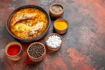 bottom view bowl of chicken soup around different spices on dark red background with copy space