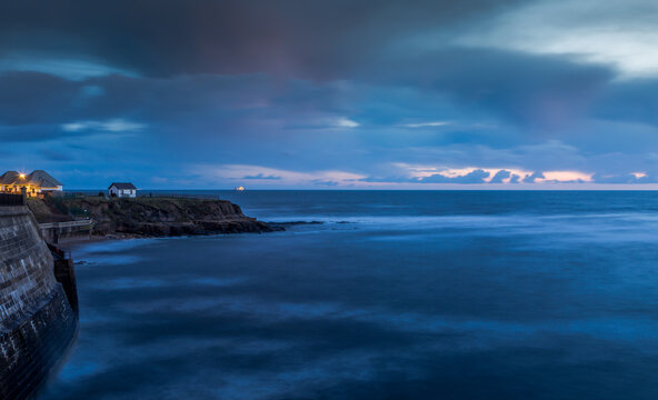 A white house on the cliffs in Cullercoats during Blue hour with clouds over-head
