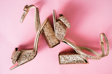Golden womens shoes with heels and sequins on pink background. 