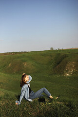 Naklejka na ściany i meble Young woman is sitting on green grass hills and feeling relax on summer sunny day