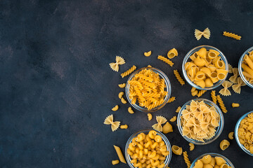 Different types of pasta on a dark concrete background. Top view, with space to copy. Concept of products, culinary backgrounds.