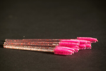 pink brushes for combing extended eyelashes on a dark background. 