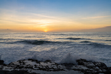 large waves crash onto rocky shore with tidal pools at sunset