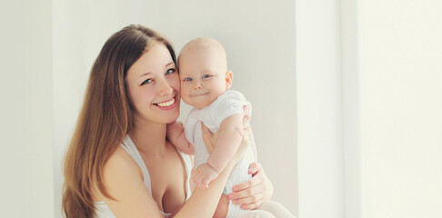 Happy smiling mother and little baby sitting together in white room at home