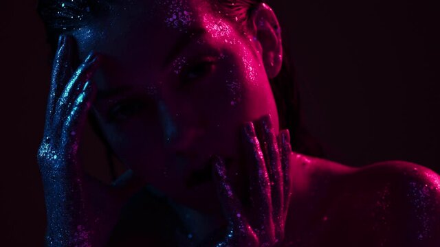 Female fashion model in sparkles in neon light posing in studio, sexy girl with glittering body art, close up video