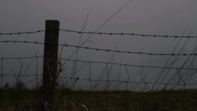 Barbed wire fence in farmers field against dark skies