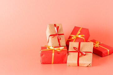 A lot of gifts wrapped in red and natural paper and tied with ribbon. Pink background