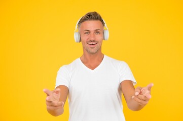 Happy middle-aged man in headphones point fingers promoting product or service yellow background, pointing