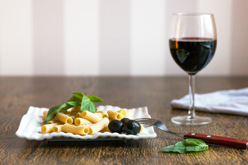 traditional italian pasta al dente with olives , basil leaves, and red wine, top view
