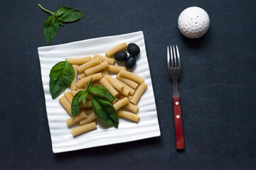 traditional italian pasta al dente with olives and basil leaves, top view, black background