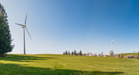 Multiple wind turbines on hill with blue sky and idyllic farm