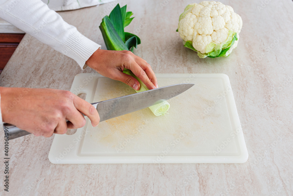 Wall mural woman cutting leek with steel knife on plastic cutting board