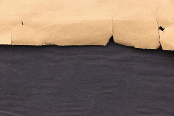 Edge of torn yellowed paper on a black surface. Black blank background.