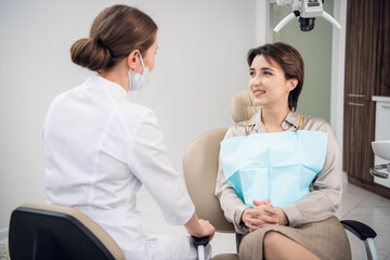 Obraz premium A portrait of a woman with a toothy smile sitting on the dental chair and talking to her doctor.