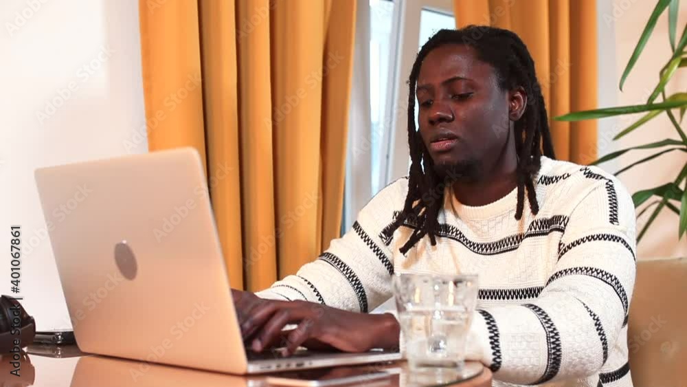 Poster afro man sitting at a table doing work using a laptop. multitasking in the office using the internet