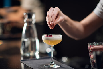 A glass with a bright yellow alcoholic cocktail on the bar and the hands of a bartender in a nightclub