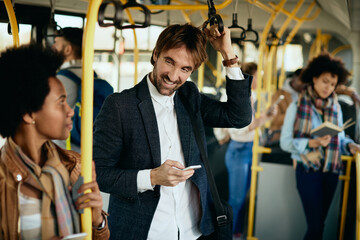 Happy man using cell phone and talking to a passenger while commuting by bus.
