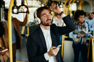 Smiling businessman listening music with eyes closed while commuting by public transport.