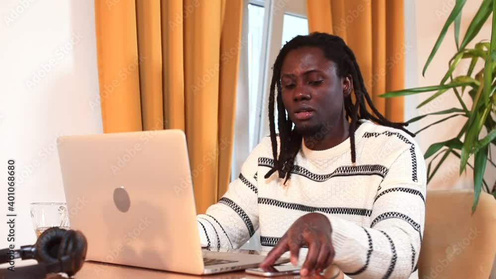 Poster afro man sitting at a table doing work using a laptop. multitasking in the office using a telephone 