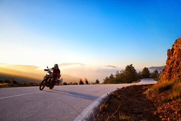 A motorcyclist taking a beautiful curve in front of a magical sunset. The sky, the trees, the...