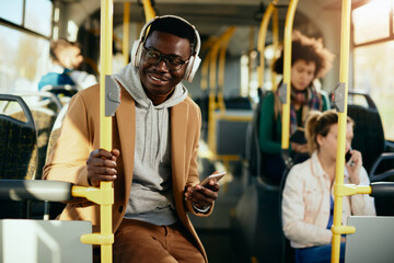 Happy African American man wearing headphones while traveling by bus.