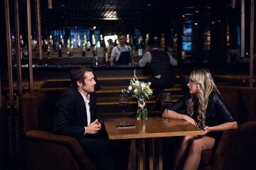 first date in a restaurant with a young man and a pretty blonde, sitting at the table, on the table a bouquet and a smartphone.
