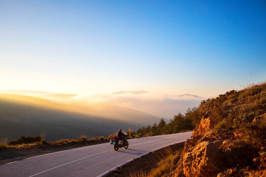 A motorcyclist taking a beautiful curve in front of a magical sunset. The sky, the trees, the motorcycle and the colors make this photo incredible.