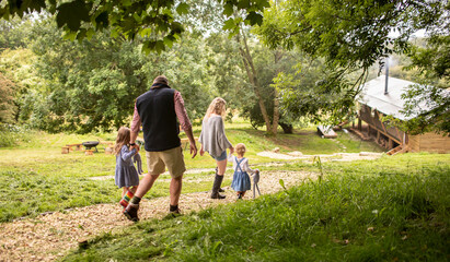 Family holding hands walking on path toward cabin in woods