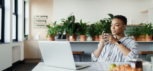 Young businesswoman with coffee working at laptop in office