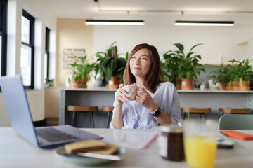 Happy businesswoman drinking coffee at laptop in office lounge