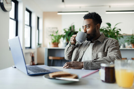 Businessman drinking coffee at laptop in morning office