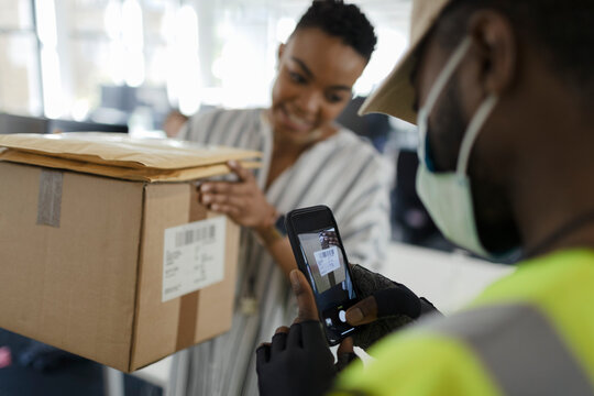 Courier in face mask with smart phone scanning package in office