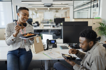 Happy business people eating takeout lunch at desk in open plan office