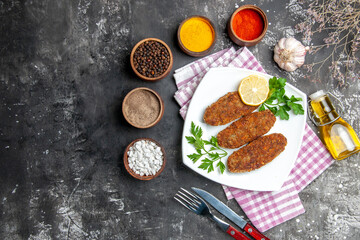 top view cutlets lemon slice parsley on white plate fork and knife spices kitchen towel on grey background with copy space