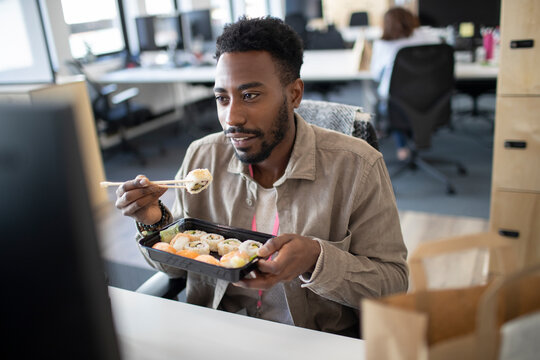 Businessman eating sushi takeout lunch at computer in office