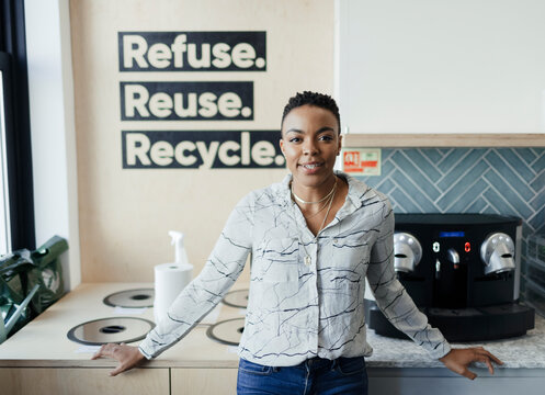 Portrait confident businesswoman at recycling bins in office kitchen