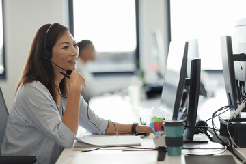 Smiling businesswoman in headset working at computer in office