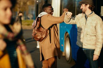 Happy men elbow bumping while greeting at bus station.