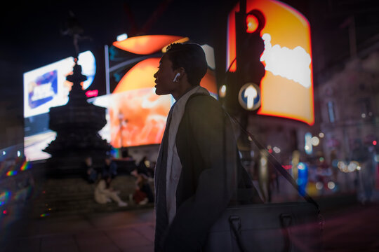 Young woman on city street corner at night, London, UK