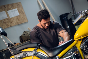 Fototapeta na wymiar A strong male biker repairs his motorcycle in the garage. Interior of the workshop