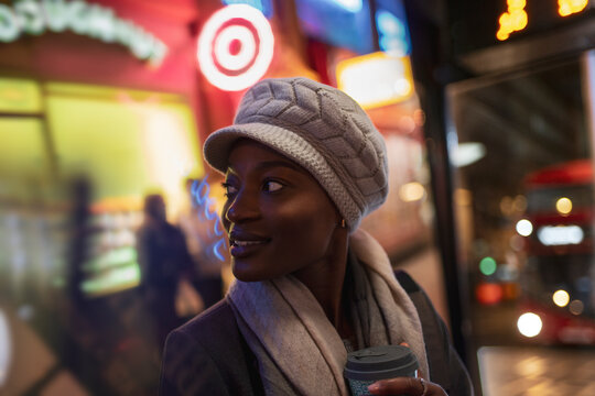 Young woman in hat on city sidewalk at night