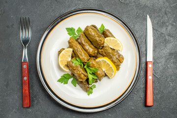 top view azerbaijani cuisine dolma with lemon slices and parsley leaves on white oval plate knife and fork on dark background