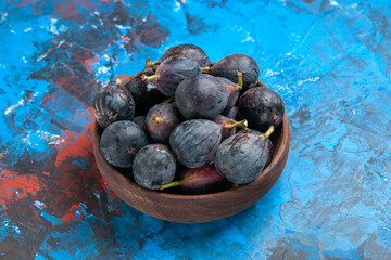 Side view of black mission figs in a small brown pot on the right side on blue background