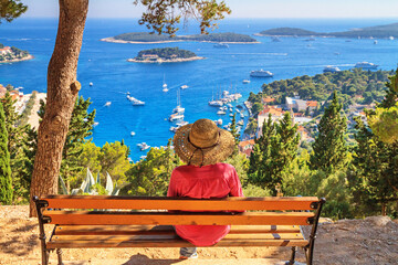 Girl tourist resting on a bench with a top view of the City Harbour and marina of the town of Hvar,...
