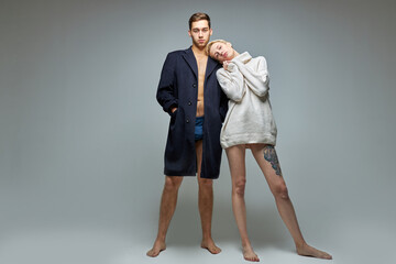 confident short-haired slim man and woman in big jacket and sweater on naked body, couple posing at camera, strange and beautiful. modern trendy people